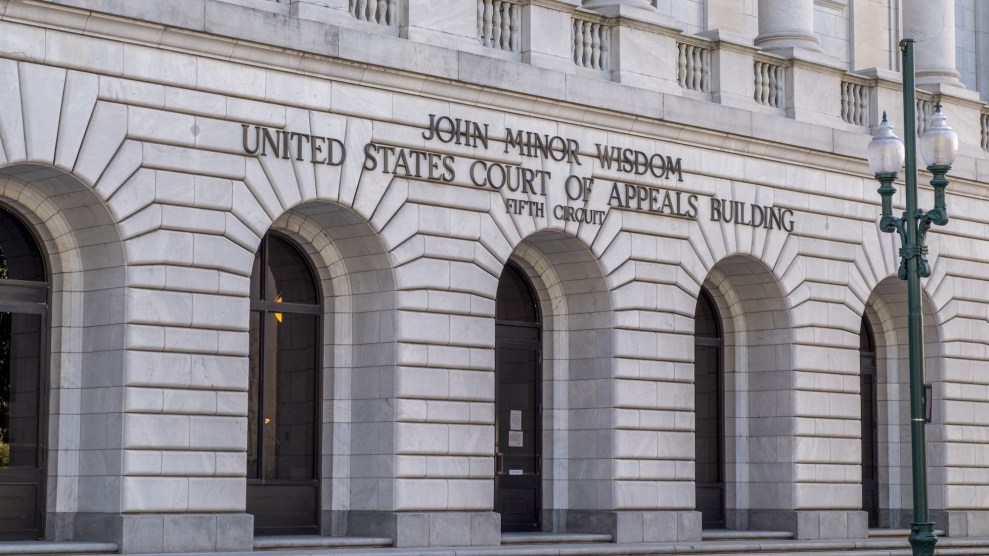 Front of a large gray-white brick court building with large exterior lettering reading "John Minor Wisdom United States Court of Appeals Building Fifth Circuit" above five arched doorways.