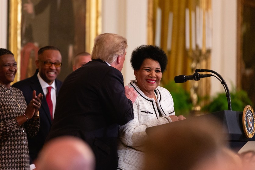 Alice Marie Johnson stands at a podium while Donald Trump talks to her.