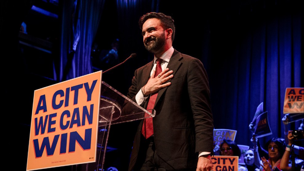 Zohran Mamdani stands, hand over his heart, behind a lectern that has a sign reading, "A city we can win"